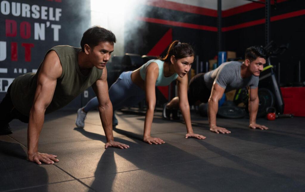 Trening obwodowy: fitnessowy "fast food" czy droga do realizacji celu? 3 zroznicowana grupa wysportowanych mezczyzn i kobiet w sportowej cwiczeniu pompek na podlodze w silowni fitness