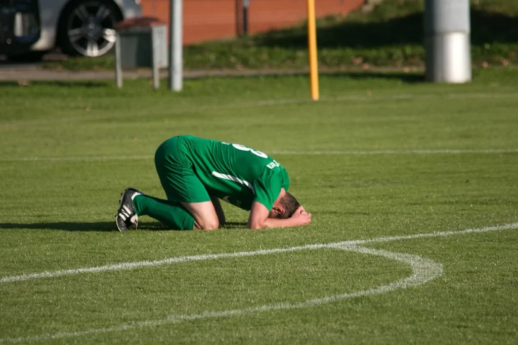 Załamany piłkarz klęczący na boisku po porażce – samokrytyka sportowców a zdrowie psychiczne