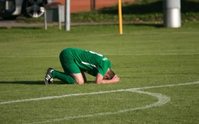 Załamany piłkarz klęczący na boisku po porażce – samokrytyka sportowców a zdrowie psychiczne