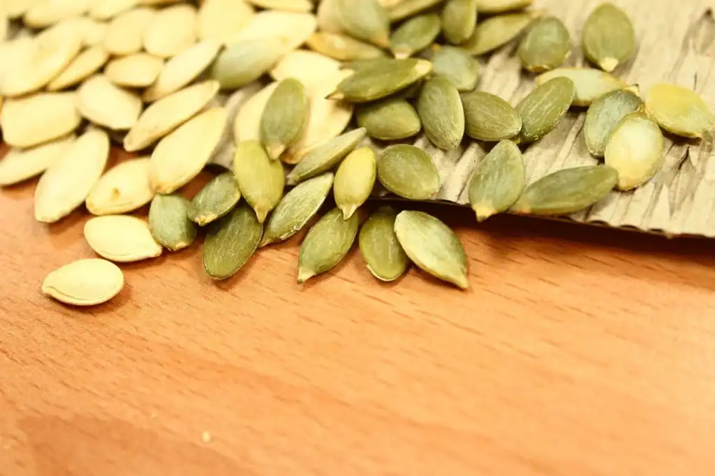 Magnez w treningu — dawkowanie, formy i kiedy ma sens suplementacja 2 Pestki dyni rozsypane na drewnie - naturalne źródło magnezu 535 mg na 100 g